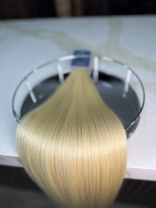 Blonde hair extensions on a clear stand with a blurred background