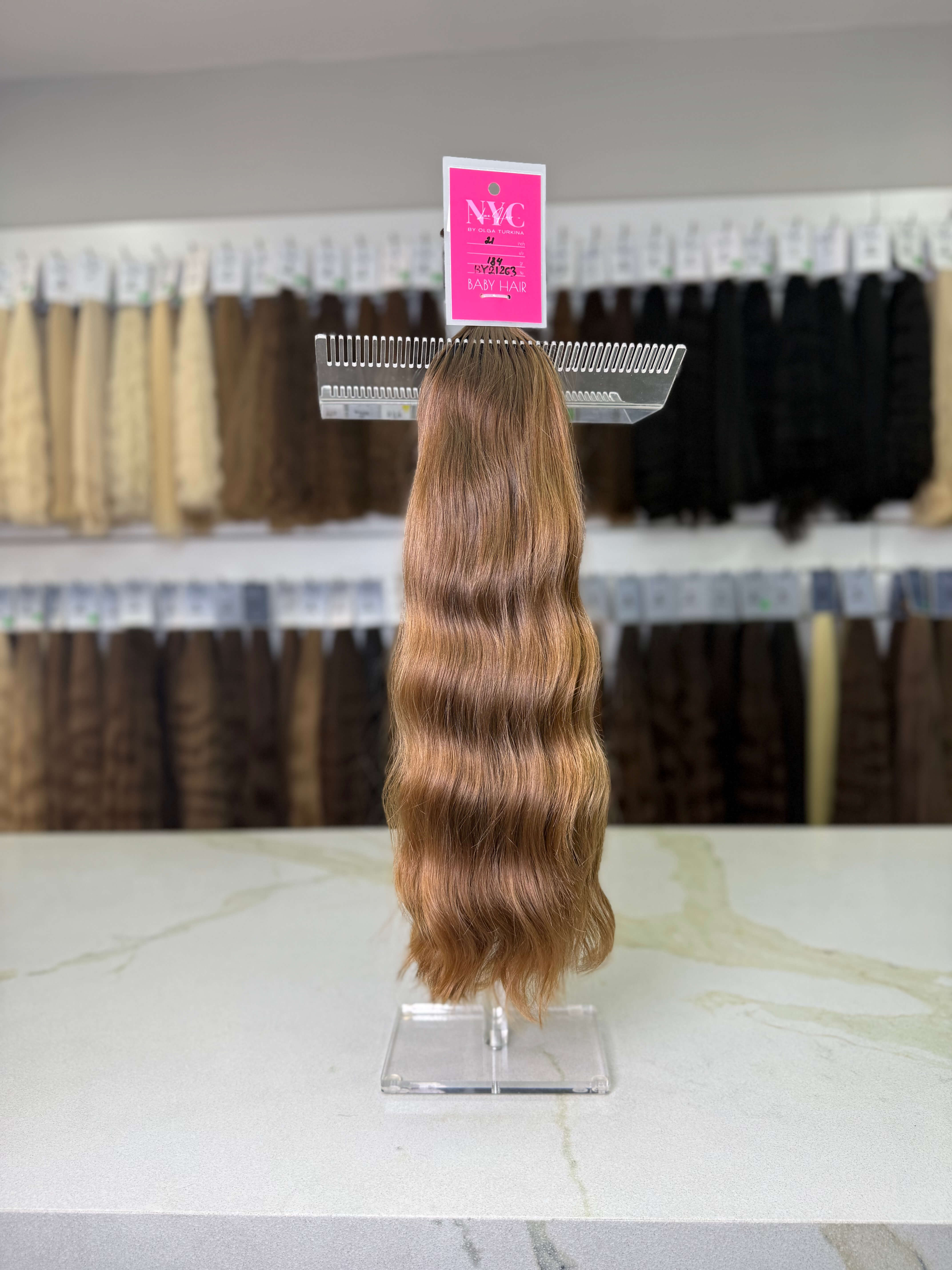 Brown hair extensions on a stand with a pink label in a store setting.