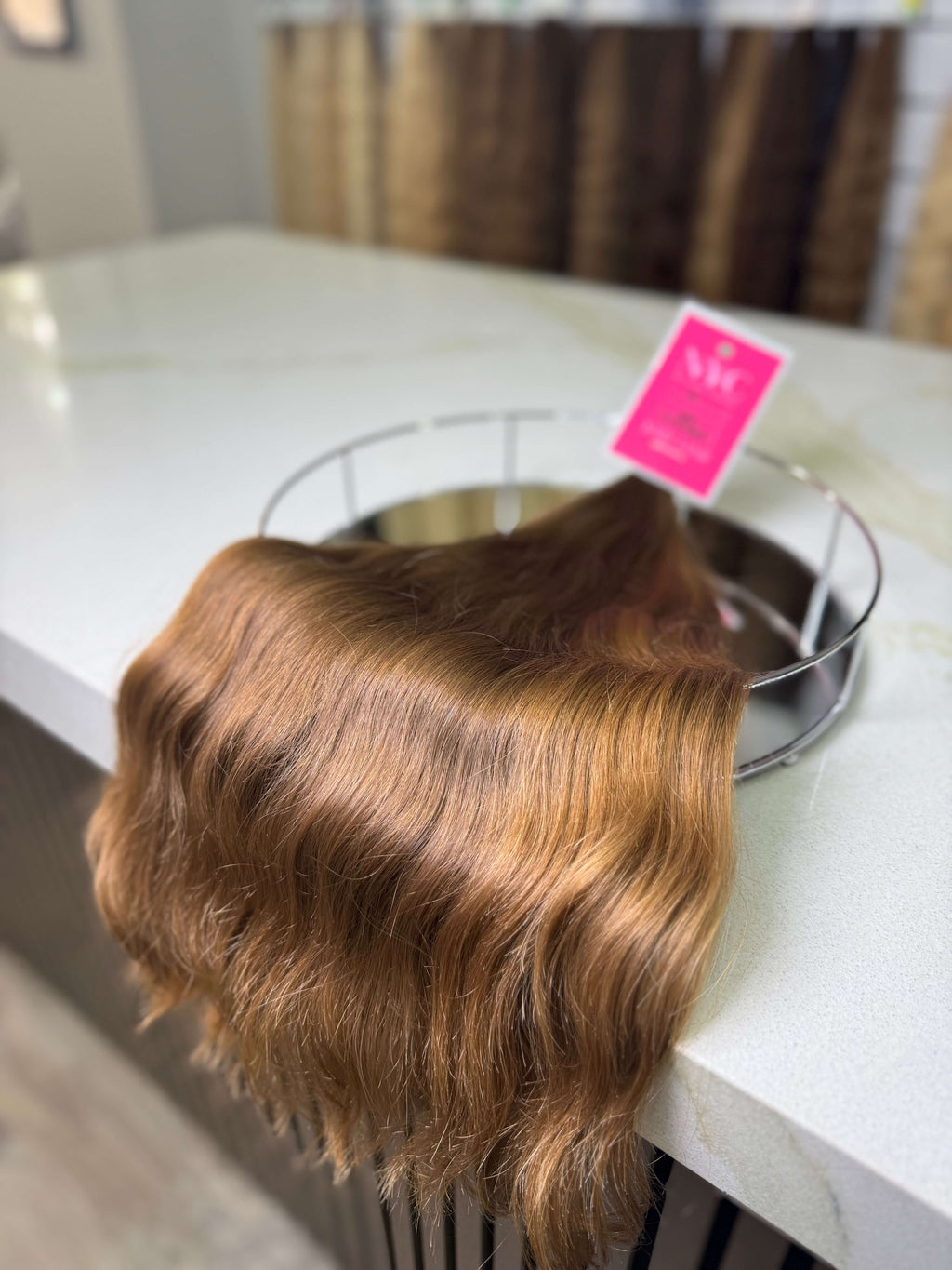 Brown hair extension on a white surface with a pink tag.