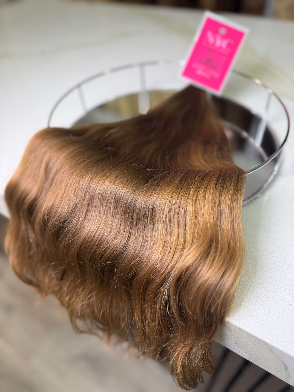 Brown hair extension on a metal stand with a pink tag in the background