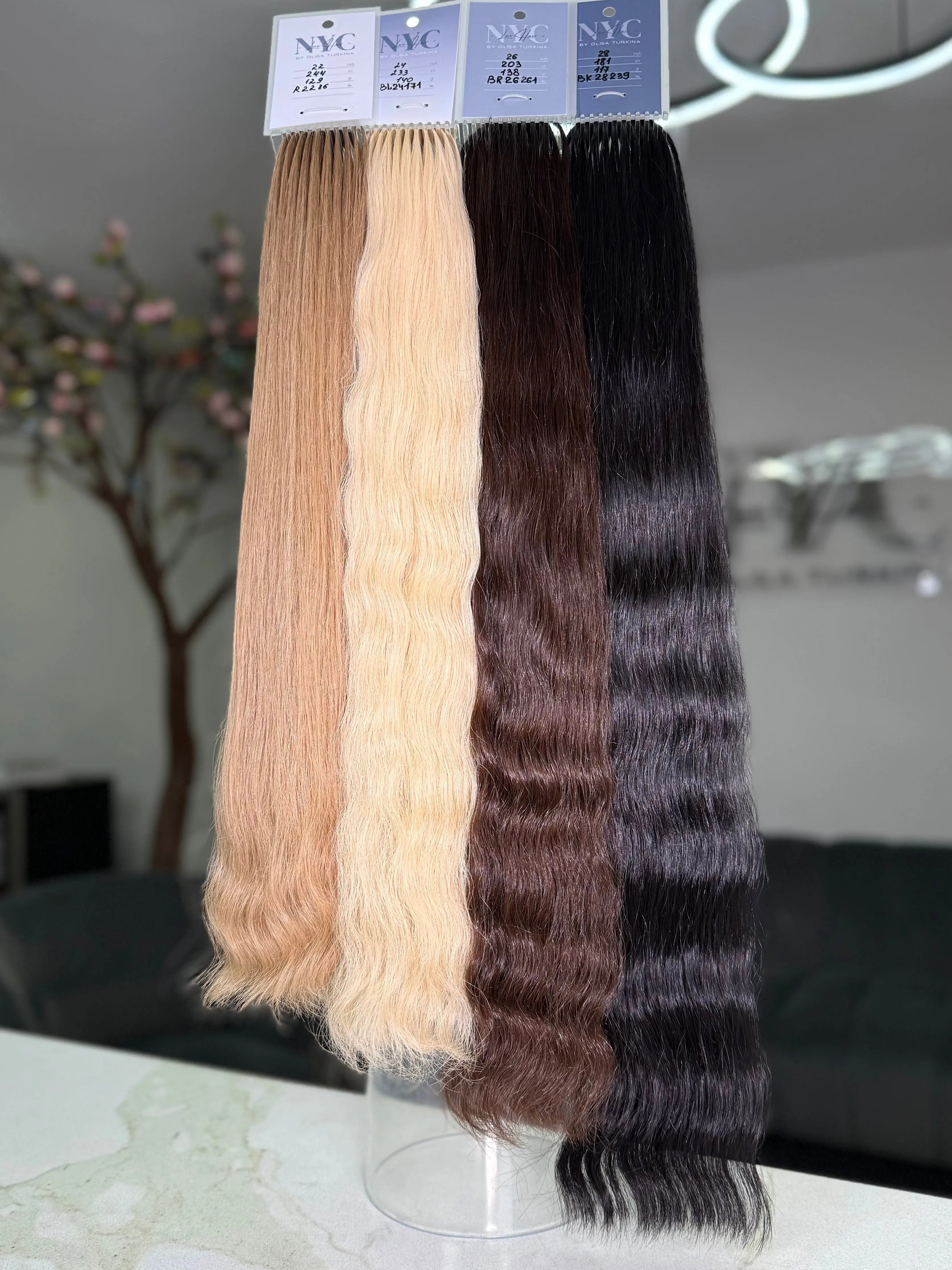 Four bundles of hair extensions in different colors on a stand with 'NYC' labels.