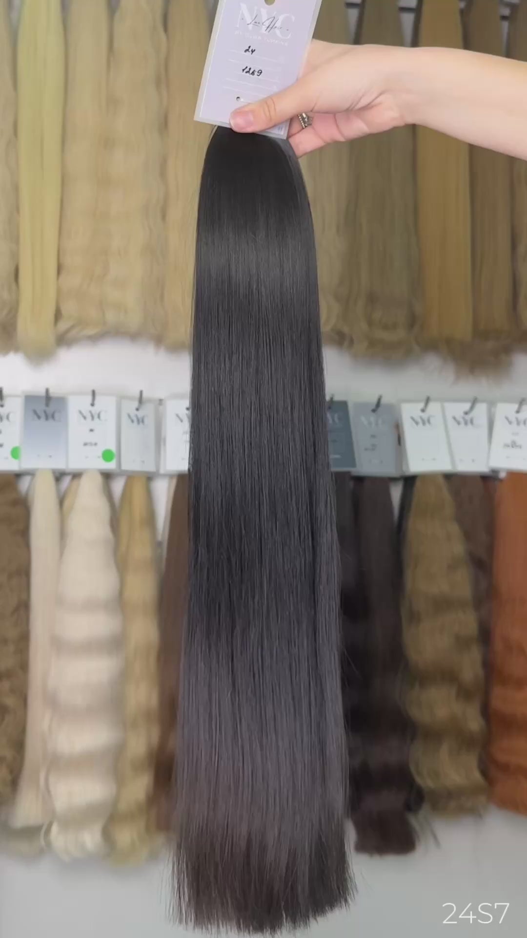 Hand holding dark brown straight hair extension color swatch #24 in front of full color bar wall, LUXHAIRNYCSHOP NYC