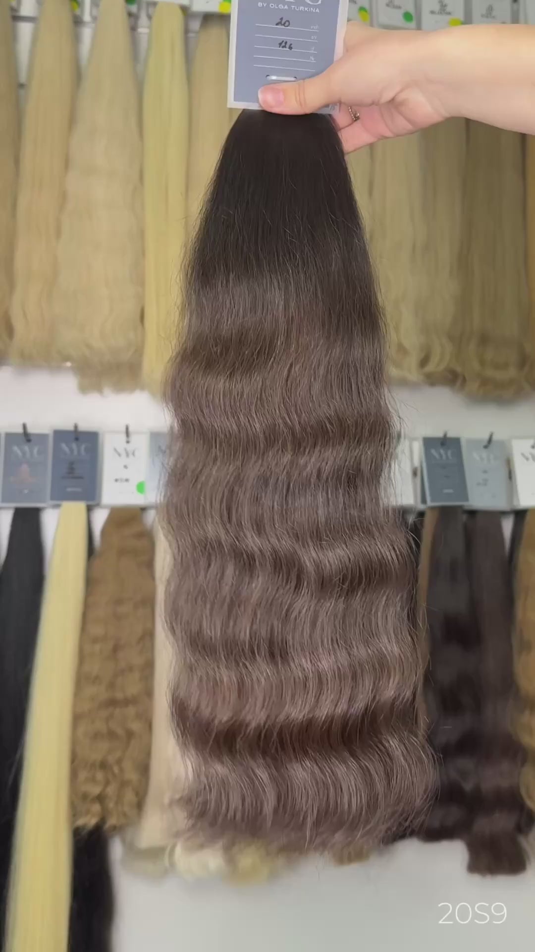 Holding light brown wavy hair extension in front of full color bar wall, LUXHAIRNYCSHOP NYC