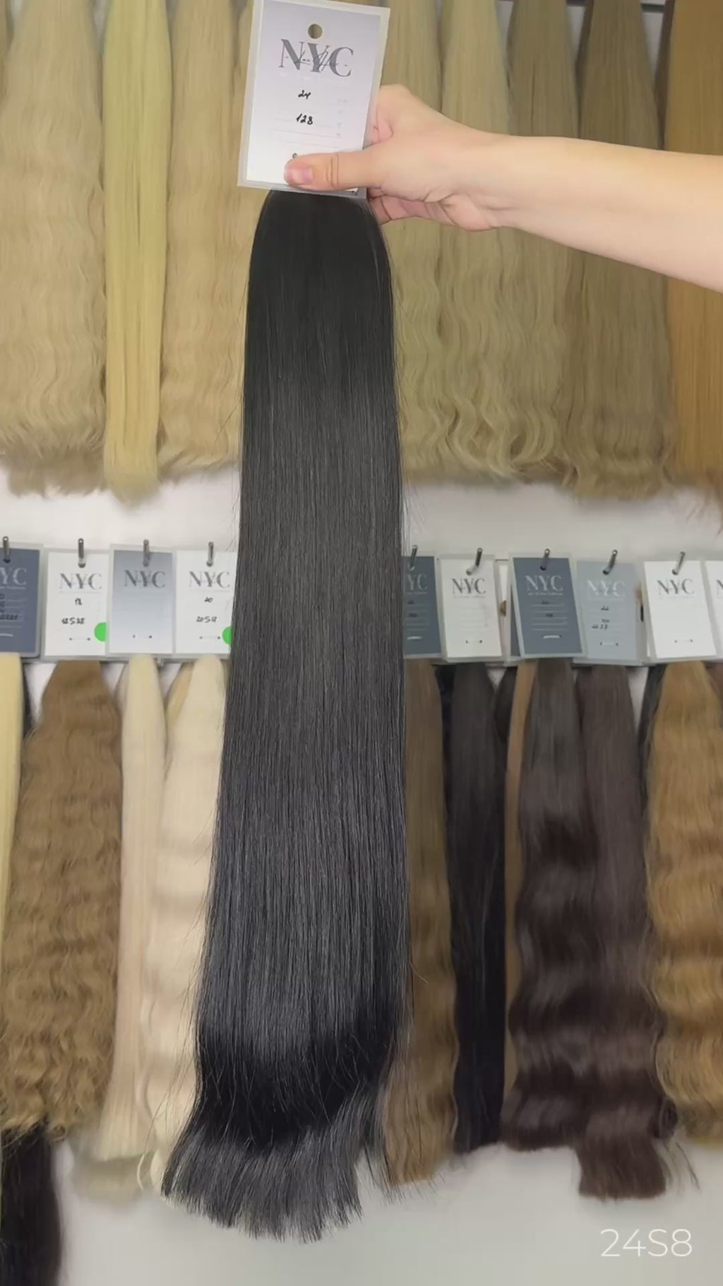Hand holding dark brown straight hair extension color swatch #24 in front of full color bar wall, LUXHAIRNYCSHOP NYC
